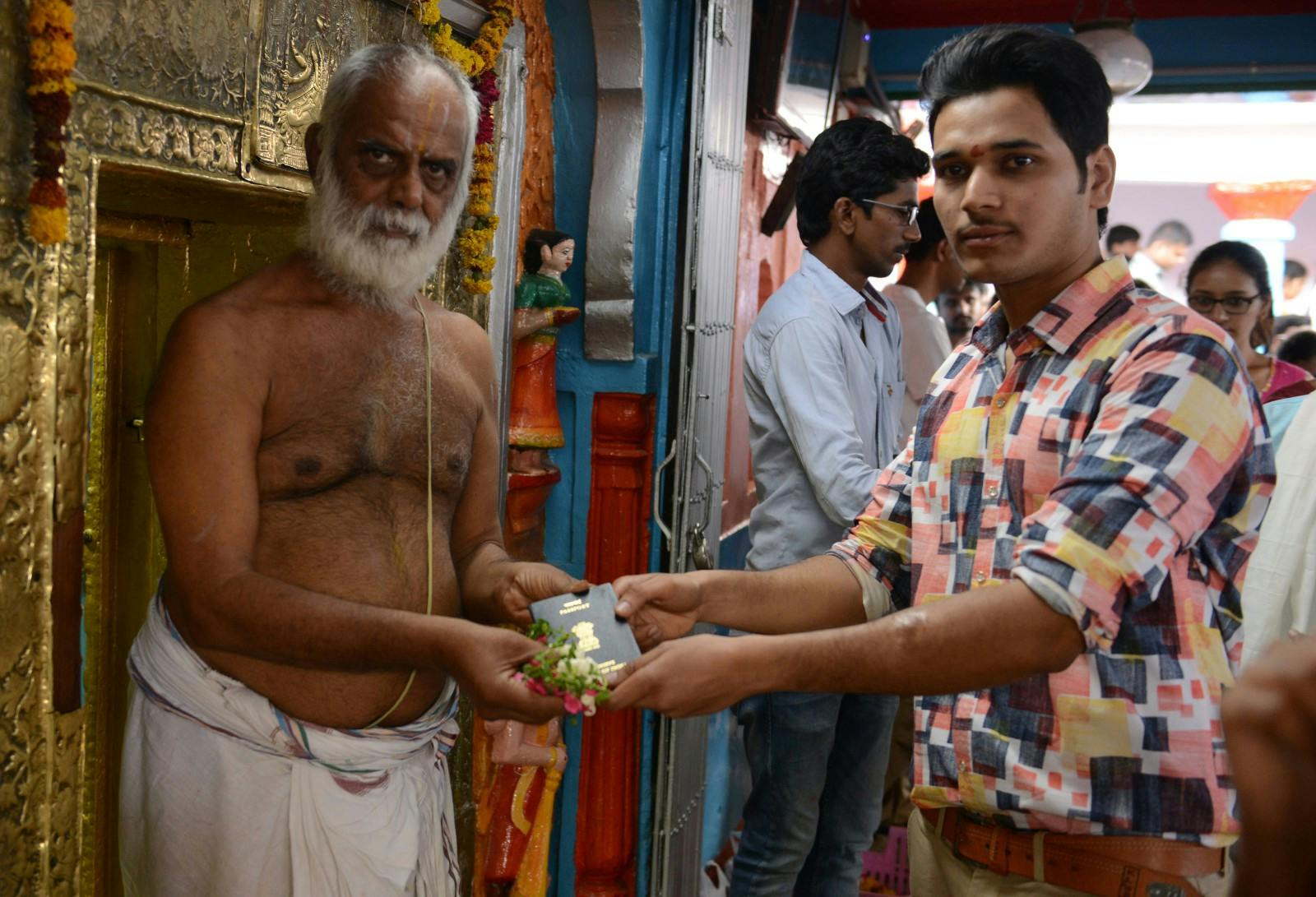 Indian Hindu devotee Rajashekar Reddy (R) receive his passport after it is blessed by a priest at the Chilkur Balaji Temple in Rangareddy, some 30 kms from Hyderabad, on April 29, 2017 (NOAH SEELAM/AFP via Getty Images)